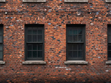 Straight-on elevation study of a brick facade — bond pattern, weathering, and window reveals under flat overcast light, no people or foreground obstruction