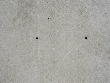 Close macro shot of raw concrete surface under north-facing daylight — aggregate texture, formwork tie holes, honest patina with no shadow ambiguity