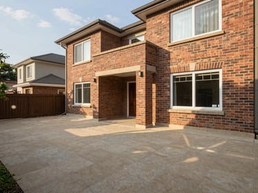 Environmental wide-angle photo of a three-bedroom house backyard showing a covered veranda with exposed brick walls, afternoon light casting soft shadows on the tiled floor, no people, no furnishings