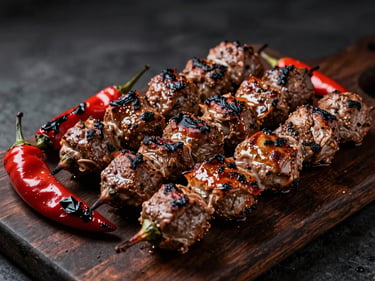 Glistening charcoal-grilled mixed kebab platter on a dark rustic board, charred peppers, moody low-key lighting