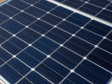 Close-up overhead shot of monocrystalline solar panel surface, blue-black cell grid with silver busbars, studio strobe lighting revealing precise cell geometry and anti-reflective coating texture