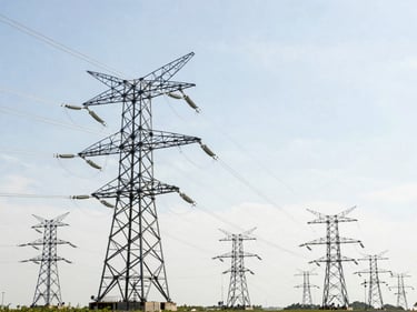 Professional industrial photograph of large electrical transmission lines spanning a landscape, under bright natural daylight, clean technical details, high-contrast realistic tones, 35mm lens