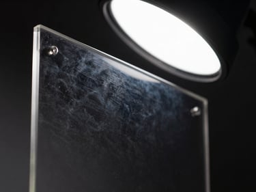 Extreme close-up of an acrylic-face print panel under studio strobe, light refracting at the polished edge, deep colour visible through the clear substrate, dark background