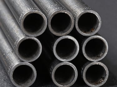 Macro overhead shot of carbon steel pipe ends arranged in a tight grid, grade markings visible on each pipe face, studio strobe lighting revealing wall thickness, dark grey surface