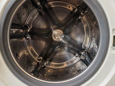 Close-up of a washing machine drum interior, metal tub ribs and rubber door seal visible, warm studio light, macro detail on the stainless steel perforations