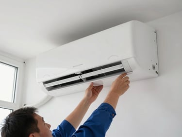 New wall-mounted split AC unit being installed on a white interior wall, technician's hands securing the mounting bracket, bright daylight from nearby window