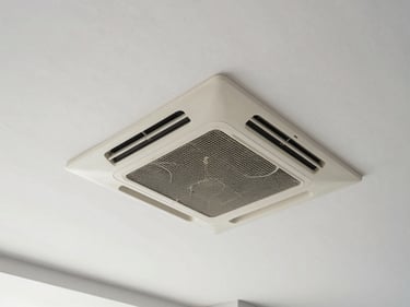 Overhead wide-angle shot of a ceiling cassette AC unit installed flush into suspended ceiling tiles, clean commercial interior, neutral daylight lighting, no people