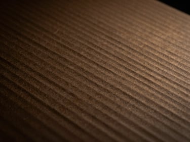 Close-up of brown corrugated cardboard texture, sharp focus, low-key moody lighting, warm gold highlights, 35mm lens, industrial discipline.