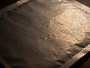 Close-up of a food-grade packaging material, clean surface, subtle texture, low-key moody lighting, warm gold highlights, 35mm lens, scale-ready.