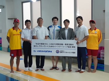 イトマンスイミングスクールと日本ライフセービング協会が『水辺の事故ゼロ』に向けたパートナーシップ協定を締結し、関係者が協定書を持って並んでいる様子