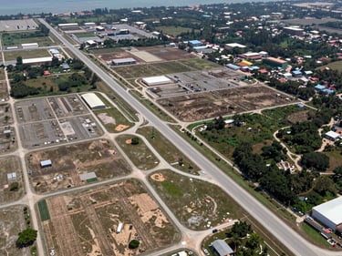 Wide environmental photograph of a Mersing coastal development zone, aerial perspective showing road infrastructure and cleared land parcels, natural daylight, no people, documentary framing
