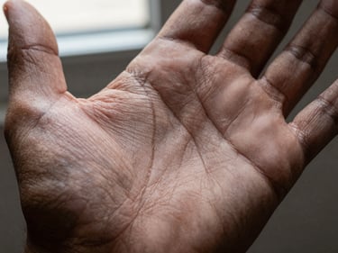 Extreme close-up of a palm center showing the head line crossing horizontally across the middle of the hand, window light from above, dark neutral background, skin tone dark brown