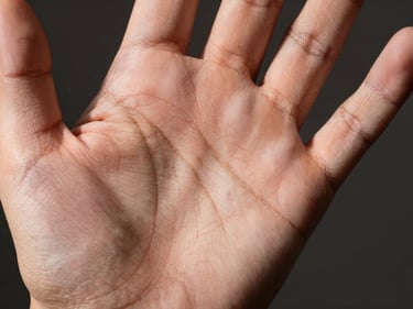 Macro close-up of the upper palm showing the heart line curving below the fingers, studio strobe raking light, strong shadow contrast in the creases, neutral dark background, light skin tone