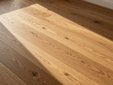 Overhead close-up of newly installed wide-plank oak hardwood flooring, natural grain and finish visible, golden-hour sidelight raking across the surface