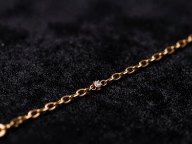 Close-up macro shot of a delicate gold bracelet with small diamonds, catching light, dark textured velvet backdrop, dramatic low-key lighting, deep black and gold tones, shallow depth of field