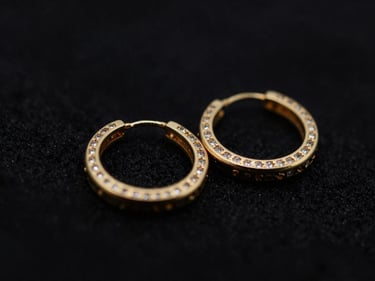 Close-up macro shot of a pair of elegant gold hoop earrings with small gemstones, dark textured backdrop, dramatic low-key lighting, deep black and gold tones, shallow depth of field