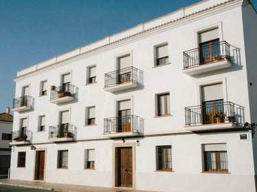 Exterior facade of a compact studio apartment block near Fuengirola beach, painted white, small juliet balconies, bright midday sun, street-level context with coastal light