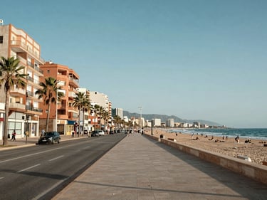 Street-level establishing shot of a seafront promenade in Fuengirola, apartment towers lining the boulevard, Mediterranean sea visible in background, clear daytime light
