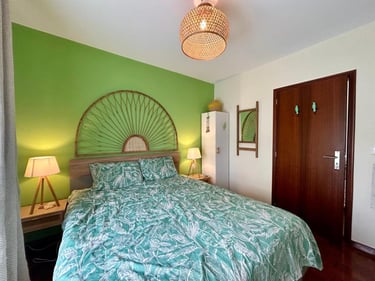 Modern bedroom featuring a green accent wall, tropical leaf bedding, and a decorative rattan sunburst headboard.