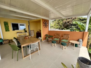 Modern outdoor patio with a wooden dining table, colorful chairs, and tropical decor overlooking lush greenery.