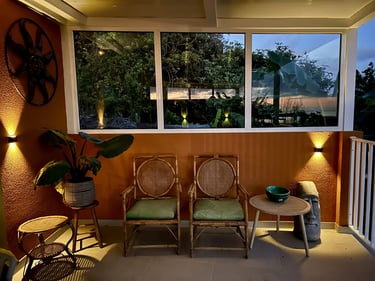Cozy covered patio at night with bamboo chairs, tropical plants, and warm outdoor wall lighting.