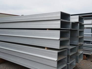 Stacked aluminum sheets and industrial scrap metal profiles, overcast outdoor light, raw texture.