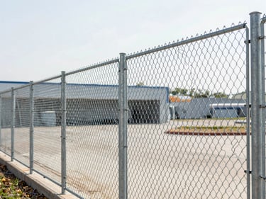 Durable galvanized chain link fence, showing tight weave and secure posts, extending into a commercial property, under bright morning daylight.