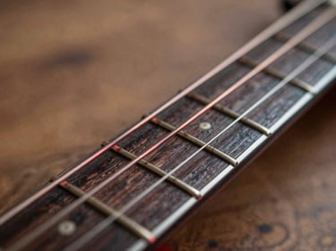 Macro shot of guitar strings over a dark wooden fretboard, crimson rim light reflecting on metal.