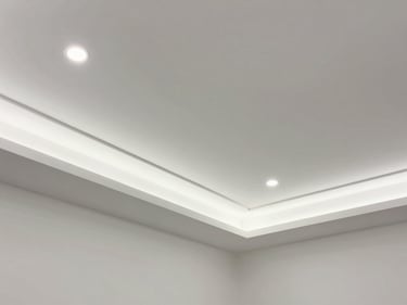 Environmental shot of a completed false ceiling installation with recessed LED lighting, geometric plaster details, photographed looking upward in an empty room, clean white finish, even diffused illumination