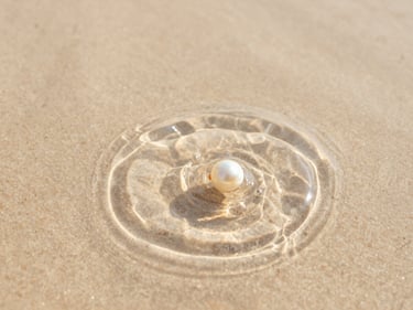 Close-up macro shot of ripples spreading in clear water over light sand, soft morning light, warm editorial photography, 35mm