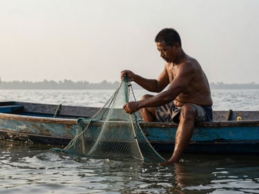 Telephoto shot of a fisherman mid-work on a flat-bottomed lagoon vessel, hands pulling a net over the gunwale, water droplets catching early morning light, the lagoon horizon compressed behind him, documentary framing, no eye contact with camera