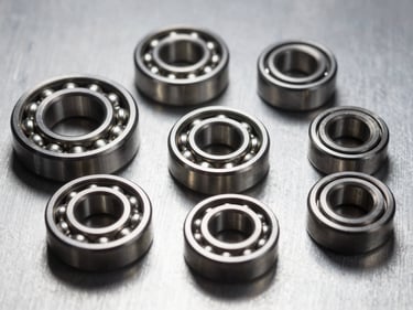 Close-up detail of precision engineering components — bearings, seals, and fasteners arranged on a brushed aluminum surface, studio strobe lighting from above, sharp metallic reflections