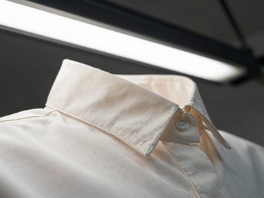 Extreme close-up of a structured women's blouse collar seam under tension on a white workbench, bright overhead fluorescent light, stitching rows visible in sharp detail, no model