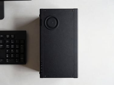 Top-down overhead shot of a small form factor desktop PC next to a keyboard on a clean desk surface, even shadowless lighting, showing compact chassis dimensions clearly