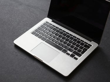 Overhead studio shot of a 15-inch business laptop open at 45 degrees on a charcoal surface, keyboard and trackpad visible, clinical even lighting, no shadows