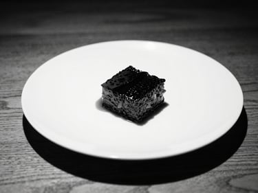 Artfully plated monochrome dish, strong shadows, clean lines, warm wood table, high-contrast lighting, 35mm lens.