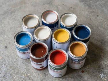 Close-up overhead flat lay of several paint cans open and stacked on a concrete warehouse floor, labels facing up, honest even studio lighting showing product volume