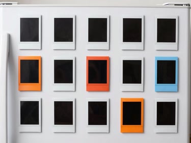 Collection of 3D printed magnetic Instax photo frames on a refrigerator, featuring various shapes and colors, clean studio lighting.