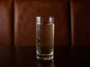 Highball glass with condensation, rich leather seating texture in background, soft amber-hued light, moody editorial photography.