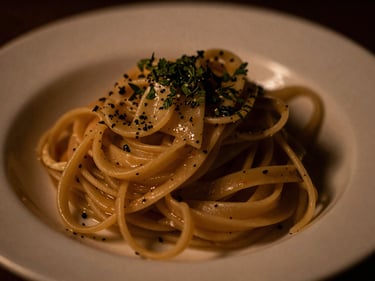 Plate of gourmet pasta with fresh herbs, soft amber lighting, intimate macro shot, moody editorial photography.