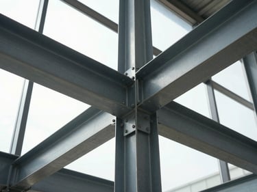 Wide environmental shot looking up along a structural steel column-and-beam connection in a commercial interior, bolted connection plate in sharp focus, diffused natural daylight from a high clerestory window revealing the steel's surface preparation