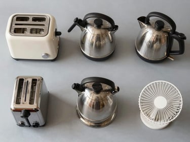 Flat-lay overhead shot of household appliances — a toaster, kettle, and small fan arranged on a neutral gray surface, bright studio lighting, no branding visible, clean product-condition context