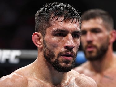 Close framing on a UFC fighter's focused face under octagon ring lighting, sweat visible, opponent blurred behind, high-contrast dramatic light