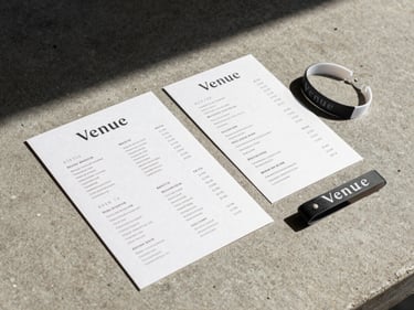 Close-up flat-lay of a venue brand identity — signage specimen, menu card, and wristband arranged on a concrete surface under north-facing daylight, precise alignment, no props