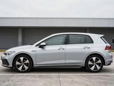 Wide three-quarter front profile of a silver hatchback parked in a clean modern parking facility, bright overcast daylight from above, no people, minimal background