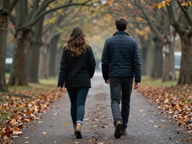 Two people walking side by side on a tree-lined path in soft overcast light, seen from slightly behind, autumn leaves on the ground, intimate medium shot