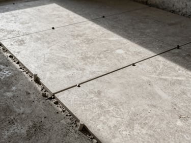 Overhead study of floor tiles being laid with spacers, grout lines perfectly aligned, mid-morning natural light on a concrete subfloor, no workers in frame
