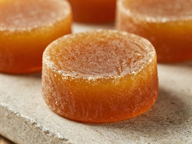 Close-up of a solid round block of golden-amber jaggery Belli on a stone counter, soft side lighting.