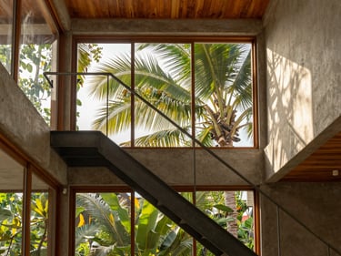 Architectural photography of a compact tropical home interior, high ceiling, natural light streaming through large windows, minimalist steel stairs