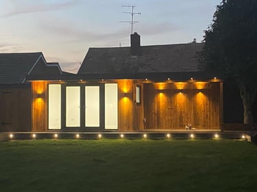 Modern timber garden room with glowing exterior LED lighting and large glass doors at dusk.
